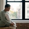 Adult in a sunlit Manhattan apartment lacing running shoes by a window, beginning a small intentional activity as part of a depression treatment plan