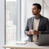 A composed professional taking a mindful pause by a large window in a modern Manhattan office