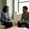 Therapist and client seated across from each other mid-session in a calm, uncluttered sage-toned office