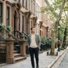Man walking along a quiet tree-lined Manhattan side street in early morning light, passing brownstone stoops